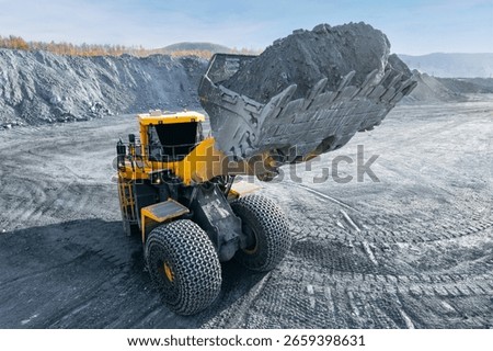 Mining large yellow backhoe loader holds full bucket of gold and copper ore at open pit mine.
