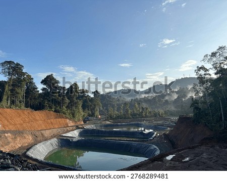 Mining site with multiple tailings ponds surrounded by forest landscape under clear blue sky. Concept of mining industry, environmental management, and land development.