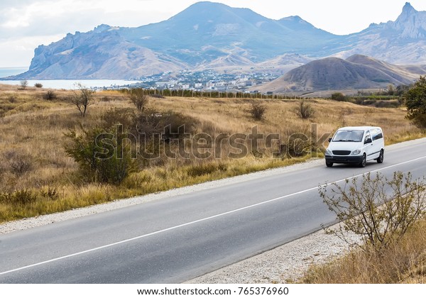 minivan is moving on a country road in a mountainous\
area near the lake