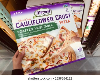 Minneapolis, MN - April 3, 2019: Caucasian Woman Shopper's Hand Holds Up A Package Of Milton’s Craft Bakers Cauliflower Crust Roasted Vegetable Pizza At A Grocery Store