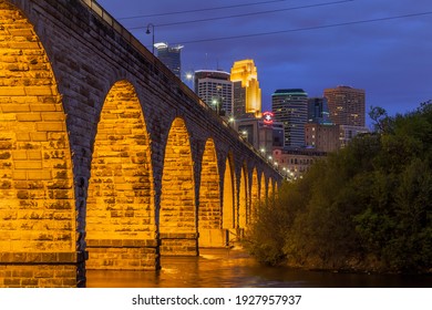MINNEAPOLIS, MN - MARCH 2016 - The Golden Stone Arch Bridge Leading to the Minneapolis Skyline Illuminated during a Spring Twilight Long Exposure