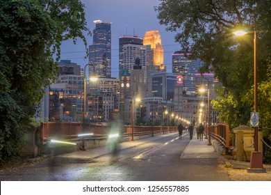 MINNEAPOLIS, MN - SUMMER 2018 - A Medium Shot of Pedestrians and Bicyclists Crossing the Stone Arch Bridge in front of the Minneapolis Skyline during Twilight