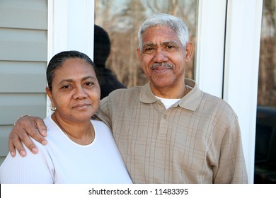 Minority couple standing in front of their home