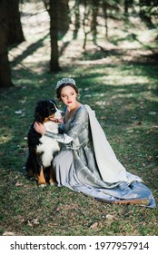 Minsk, Belarus - 04.14.2020. Young Glam Beautiful Lady Wearing Luxurious Gown And Coat Standing In A Woods With Her Dog.