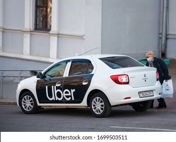 Minsk, Belarus. Apr 2020. Elderly Woman In Medical Mask On Her Face Gets Into Uber Taxi Car. Masked Passenger Gets Into Taxi During Virus Outbreak