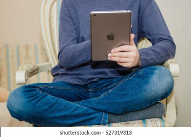 Minsk, Belarus - December 1, 2016: Teenager schoolboy sitting on a chair and reading a book on iPad. Company logo Apple. The hottest gadgets. Popular technical trends. Modern training. E-learning.