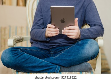 Minsk, Belarus - December 1, 2016: Teenager Schoolboy Sitting On A Chair And Reading A Book On IPad. Company Logo Apple. The Hottest Gadgets. Modern Training.