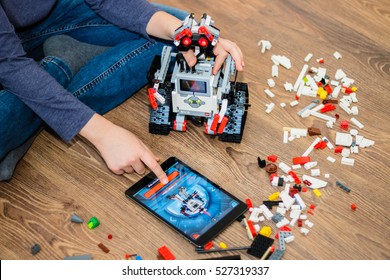 Minsk, Belarus - December 1, 2016: Teenager schoolboy sitting on the floor and controls the robot  Walle with iPad. Lego EV 3. School Robotics. Modern training. The hottest gadgets.