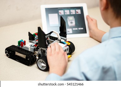 Minsk, Belarus - December 29, 2016: Teenager Schoolboy Sitting On The Table And Controls The Robot  Car With IPad. Lego EV 3. Mindstorms. School Robotics. Modern Training. The Hottest Gadgets.