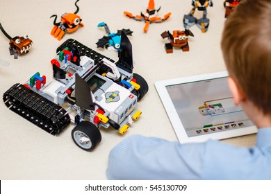 Minsk, Belarus - December 29, 2016: Teenager Schoolboy Sitting On The Table And Controls The Robot  Car With IPad. Lego EV 3. Mindstorms. School Robotics. Modern Training. The Hottest Gadgets.