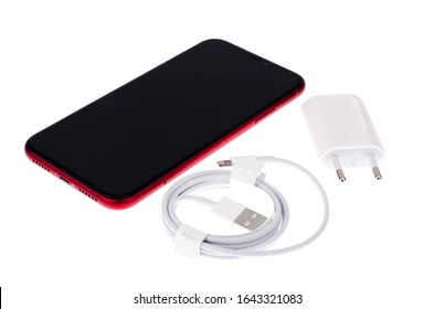 Minsk, Belarus - December 4, 2019: Iphone - Mobile phone in red case, charger on white background. Belongs to the American corporation Apple.