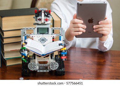 Minsk, Belarus -  February 11, 2017: Lego Robot Reading A Book. Pile Of Books In The Background. Robot In The Library.  Teenager Read The Book On Ipad Apple. School. E-learning.  STEM Education.