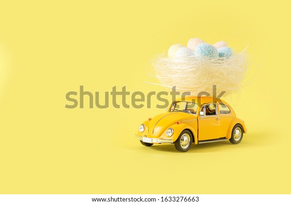 Minsk, Belarus - February 2020: Easter\
holiday. A yellow toy car carries a nest with colorful eggs on a\
yellow background. Easter holiday card with retro\
car