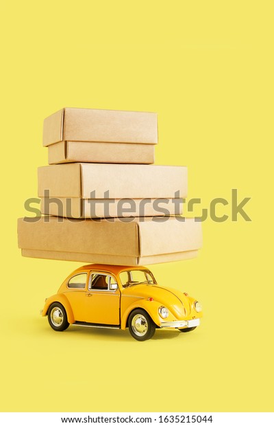 Minsk, Belarus -\
February 2020: Zero waste eco friendly packaging, transportation of\
goods, eco business. A yellow toy car carries Kraft boxes on a\
yellow background.