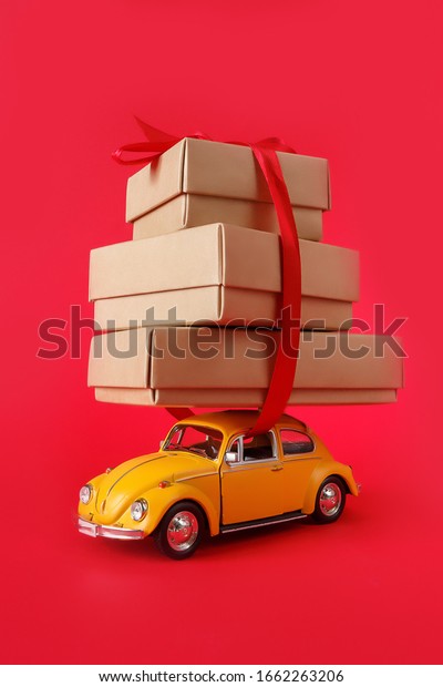 Minsk, Belarus -\
February 2020: Zero waste eco friendly packaging, transportation of\
goods, eco business. A yellow toy car carries Kraft boxes on a red \
background.