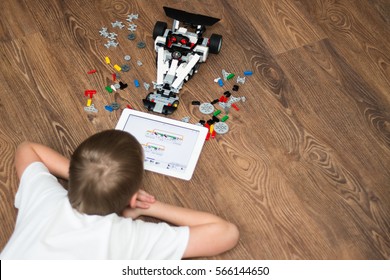 Minsk, Belarus - January 24, 2017: Teenager Schoolboy Sitting On The Floor And Controls The Robot  Car With IPad. Lego EV 3. School Robotics. Modern Training. The Hottest Gadgets. E-learning.