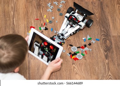 Minsk, Belarus - January 24, 2017: Teenager Schoolboy Sitting On The Floor And Controls The Robot  Car With IPad. Lego EV 3. School Robotics. Modern Training. The Hottest Gadgets. E-learning.