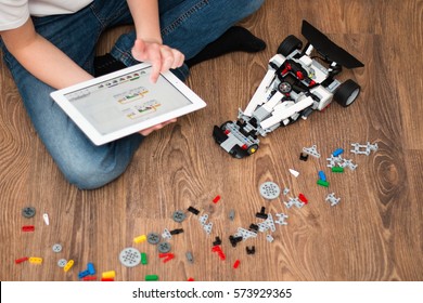 Minsk, Belarus - January 24, 2017: Teenager Schoolboy Sitting On The Floor And Controls The Robot  Car With IPad. Lego EV 3. School Robotics. Modern Training. E-learning. STEM Education.