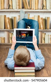 Minsk, Belarus - January 3, 2017: Boy teenager is on the floor and plays Minecraft game on iPad Apple. E-learning. Modern technology in education. Books.