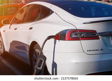 Minsk, Belarus. Mar 2022. Tesla Model S, EV electric car charging. EV vehicle plugged getting electricity from power station. White Tesla Model S car charging 