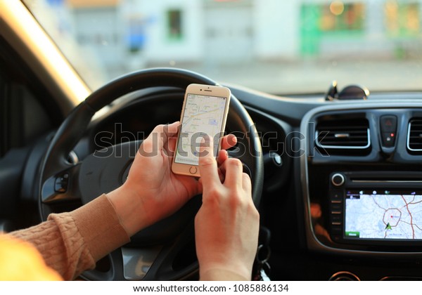 MINSK, BELARUS - MAY 05, 2018: The man in the car\
is holding the Google Maps application on new white Apple iPhone 7.\
Google Maps is most popular mapping service for mobile provided by\
Google.