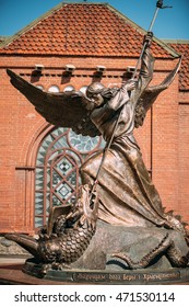 Minsk, Belarus - May 20, 2015: Statue Of Archangel Michael With Outstretched Wings, Thrusting Spear Into Dragon near Red Catholic Church Of Sts. Simon And Helena On Independence Square