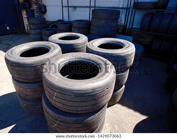 Minsk, Belarus - May 2019. Used car tyres pile in\
warehouse at repair shop. New and used tires stacked in outdoor\
warehouse, aqiting for instalation on trucks. Used lorry tires at\
tire shop.