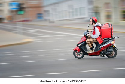 Minsk, Belarus. May 2020. Delivery boy in protective helmet on moto scooter riding fast on the road, delivering online food and grocery orders to customers. Food courier, delivery service Menu.by - Shutterstock ID 1782064412