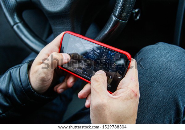 Minsk, Belarus -\
october 10, 2019: Hands holding smartphone with Call of Duty Mobile\
game. The gameplay on iPhone 7 from the first person view, the\
driver plays in the car.