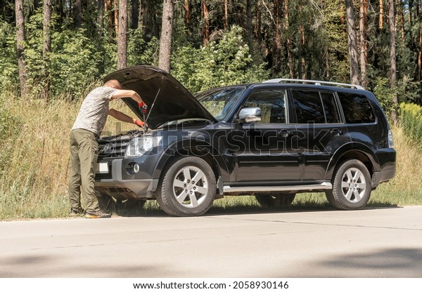 MINSK, BELARUS -\
October 17 2021 Driver standing and looking in hood raised up after\
car break in road trip.
