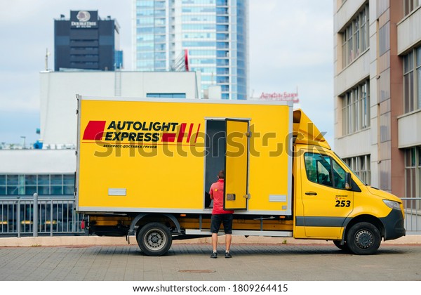 Minsk, Belarus. Sep 2020.  Post courier in red\
uniform near yellow delivery van with company logo. Autolight\
Express LLC largest courier, parcel, and express mail service in\
Belarus delivery\
industry