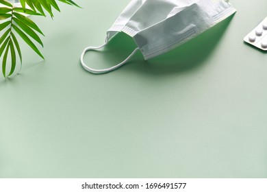 Mint green background with face mask, pills and natural palm tree leaf. Space for your text, copy-space. Social isolation, hygiene, prophylactic measures to fight novel coronavirus. - Shutterstock ID 1696491577
