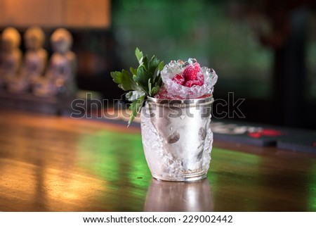 Mint julep cocktail with raspberry served in frozen metal cup on the bar