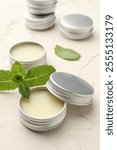 Mint lip balms and green leaves on beige textured table, closeup. Cosmetic product