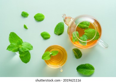 Mint tea. Flat lay teapot and teacup with green mint leaves on green background. Top view herbal beverage.