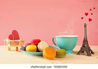 Mint vintage cup of coffee and colorful macaron or macaroon next to Eiffel Tower on wooden table over pink background
