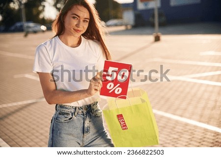 Minus fifty percent sale. Half the price. Beautiful woman in casual clothes is holding shopping bags, outdoors.
