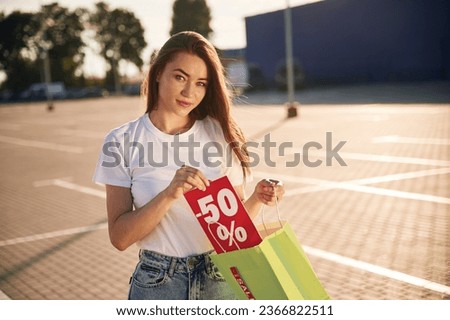 Minus fifty percent sale. Half the price. Beautiful woman in casual clothes is holding shopping bags, outdoors.
