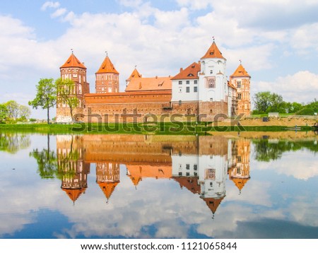 Mir, Belarus. Castle Complex Mir reflected in lake On Sunny Day with blue sky Background. Old medieval Towers and walls of traditional fort from unesco world heritage list