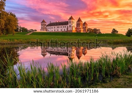 Mir Castle in Belarus at sunset with a dramatic sky and clouds. Landscape of an old castle against beautiful sky by river in autumn