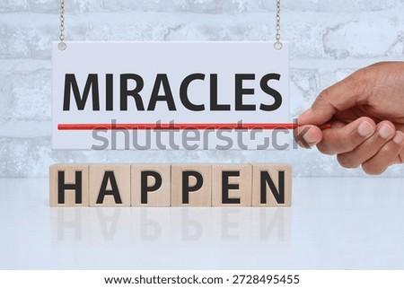 Miracles Happen Message on white board and wood blocks with hand holding red pointer in front of brick wall