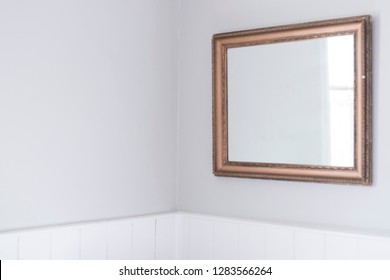 Mirror isolated on blank wall in country cottage with reflection of nearby window, lit by natural light