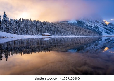 Mirror like reflection in the calm water at the famous Lake Louise in Alberta, Canada.  Sunrise colors glowing in the fog on a calm winter morning creating a beautiful natural symmetrical image