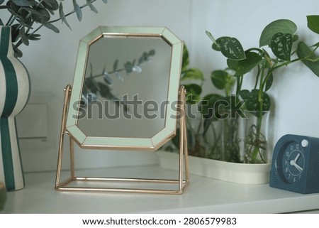 A mirror is placed on a shelf next to green plants and a clock.