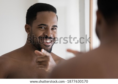 Mirror reflection close up head shot naked smiling 30s young african ethnicity man pointing finger looking at camera, enjoying starting energetic day after morning cleaning routine in bathroom.