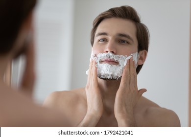 Mirror Reflection Head Shot Close Up Young Man Applying Shaving Foam, Standing In Bathroom, Handsome Satisfied Male Doing Personal Hygiene, Skincare And Morning Routine Procedure At Home