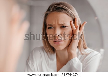 Mirror reflection of upset young lady looking at mirror and touching her forehead, having oily or dry skin problem, first wrinkles concept, bathroom interior
