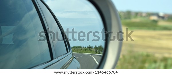 Mirror reflection of winding highway captured in\
the rear view mirror.