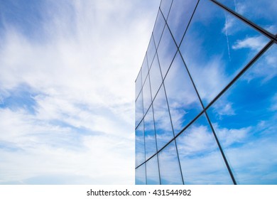 Mirrored Glass Of Corporate Office Building Reflecting A Blue Sky With Cloud Puffs