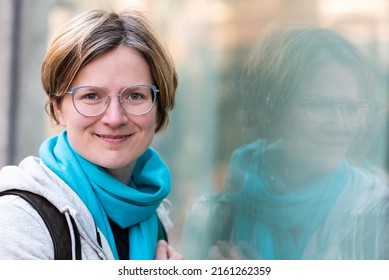 Mirrored portrait of a 35 year old white woman , standing against a glass window